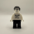 A custom Lego minifigure with black hair, a white shirt printed with the text 'BILLIONS MUST SMILE' in black, and black pants, standing against a plain light gray background.
