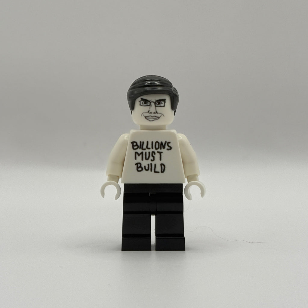 A custom-built toy minifigure resembling a LEGO figure, featuring a white torso printed with the text 'BILLIONS MUST BUILD' in black, black hair, and black legs, set against a plain light gray background.