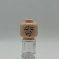 A small beige plastic head piece with a simple black face drawing, mounted on a clear acrylic stand against a light gray background.