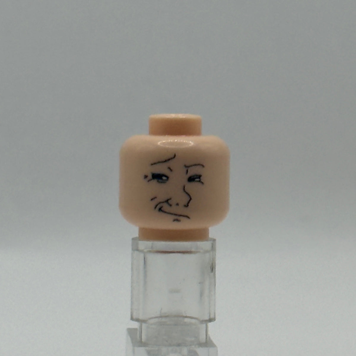 A small beige plastic head piece with a simple black face drawing, mounted on a clear acrylic stand against a light gray background.