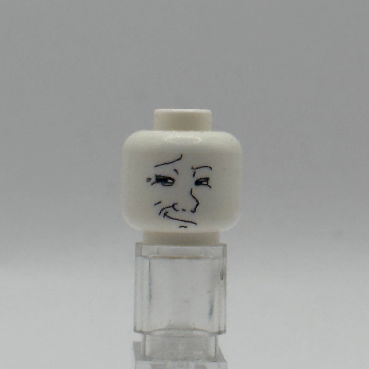 A white plastic toy head with a black hand-drawn face, mounted on a clear plastic stand against a neutral gray background.