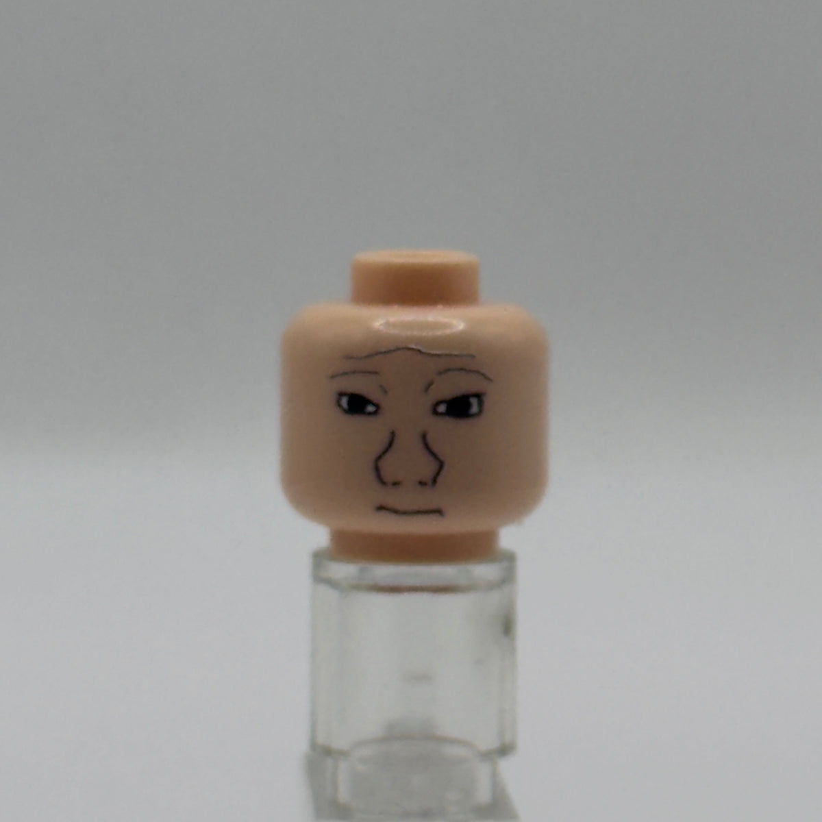 A small plastic toy head with a printed face, mounted on a clear stand against a plain light gray background.
