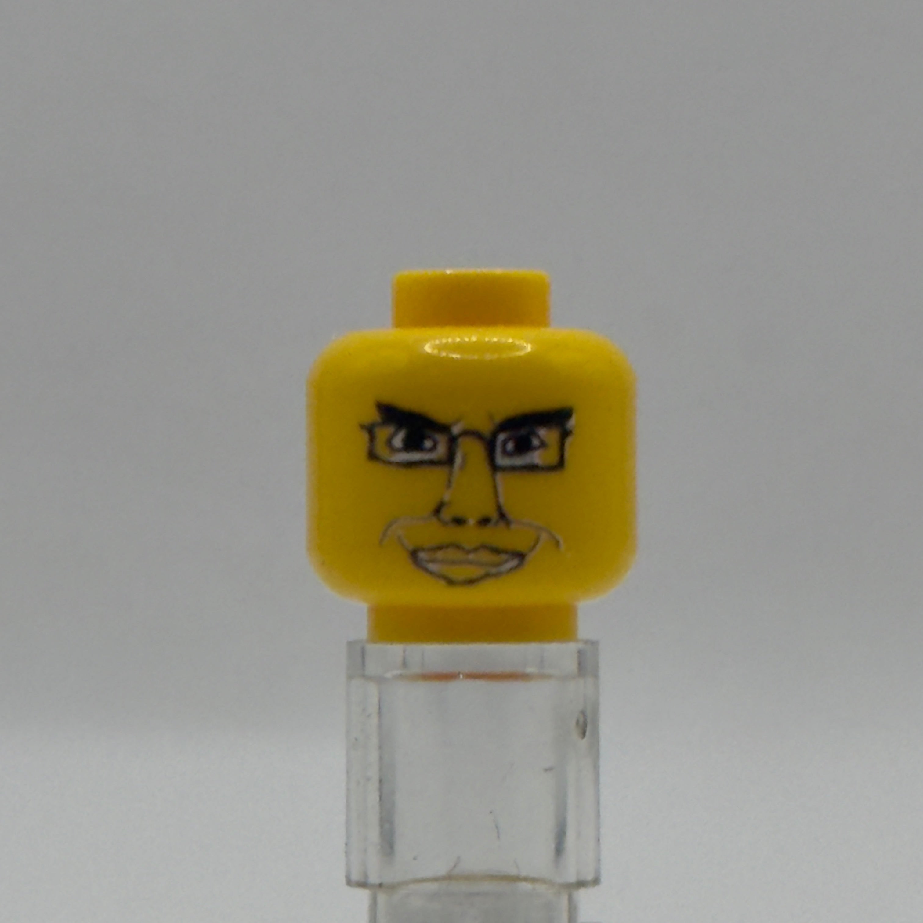 A custom yellow LEGO minifigure head with a printed face and glasses, mounted on a clear plastic display stand against a neutral gray background.
