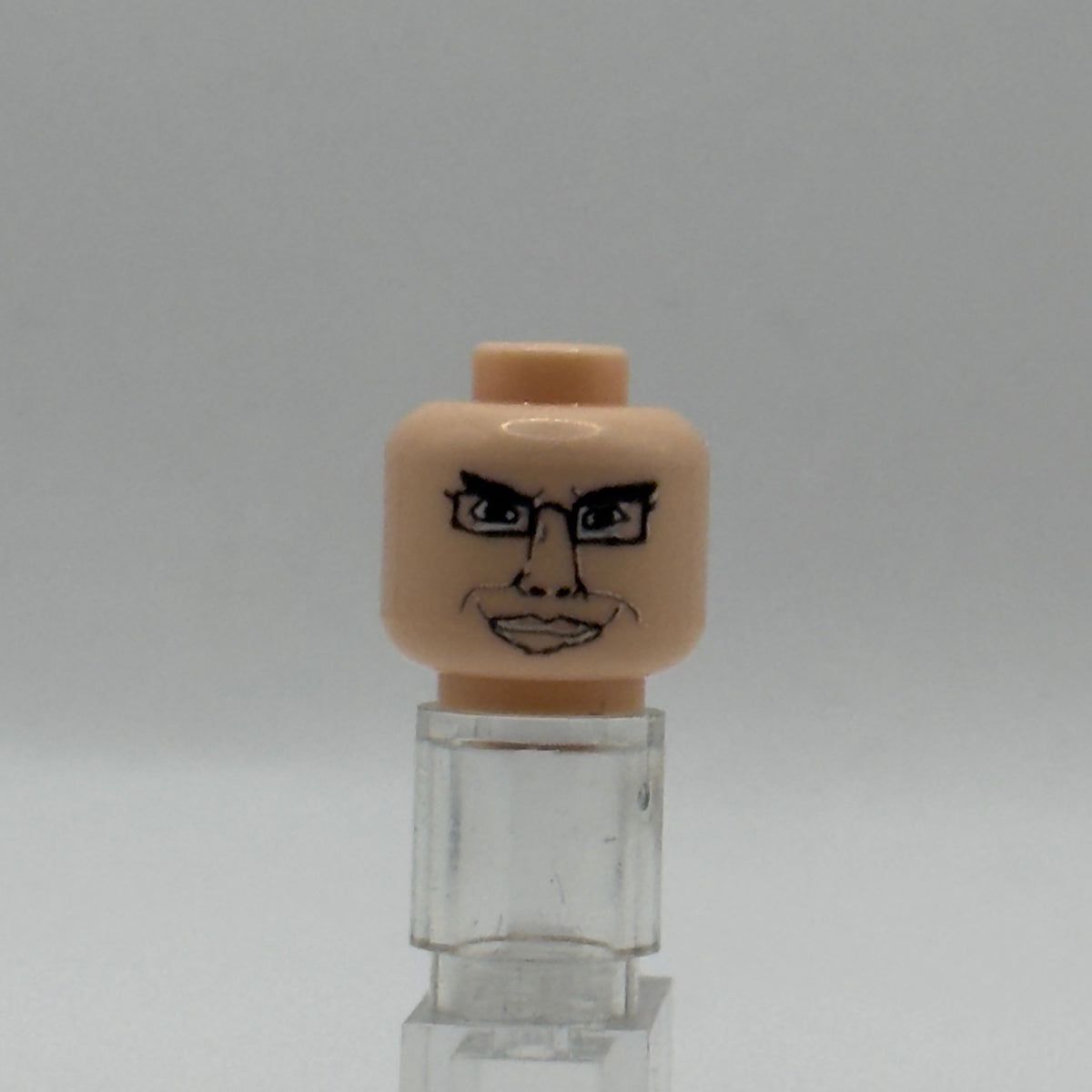 A custom-painted LEGO minifigure head with a drawn angry face and glasses, mounted on a clear plastic display stand against a neutral gray background.