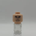 A beige plastic toy head with a printed angry face, displayed on a clear acrylic stand against a neutral gray background.